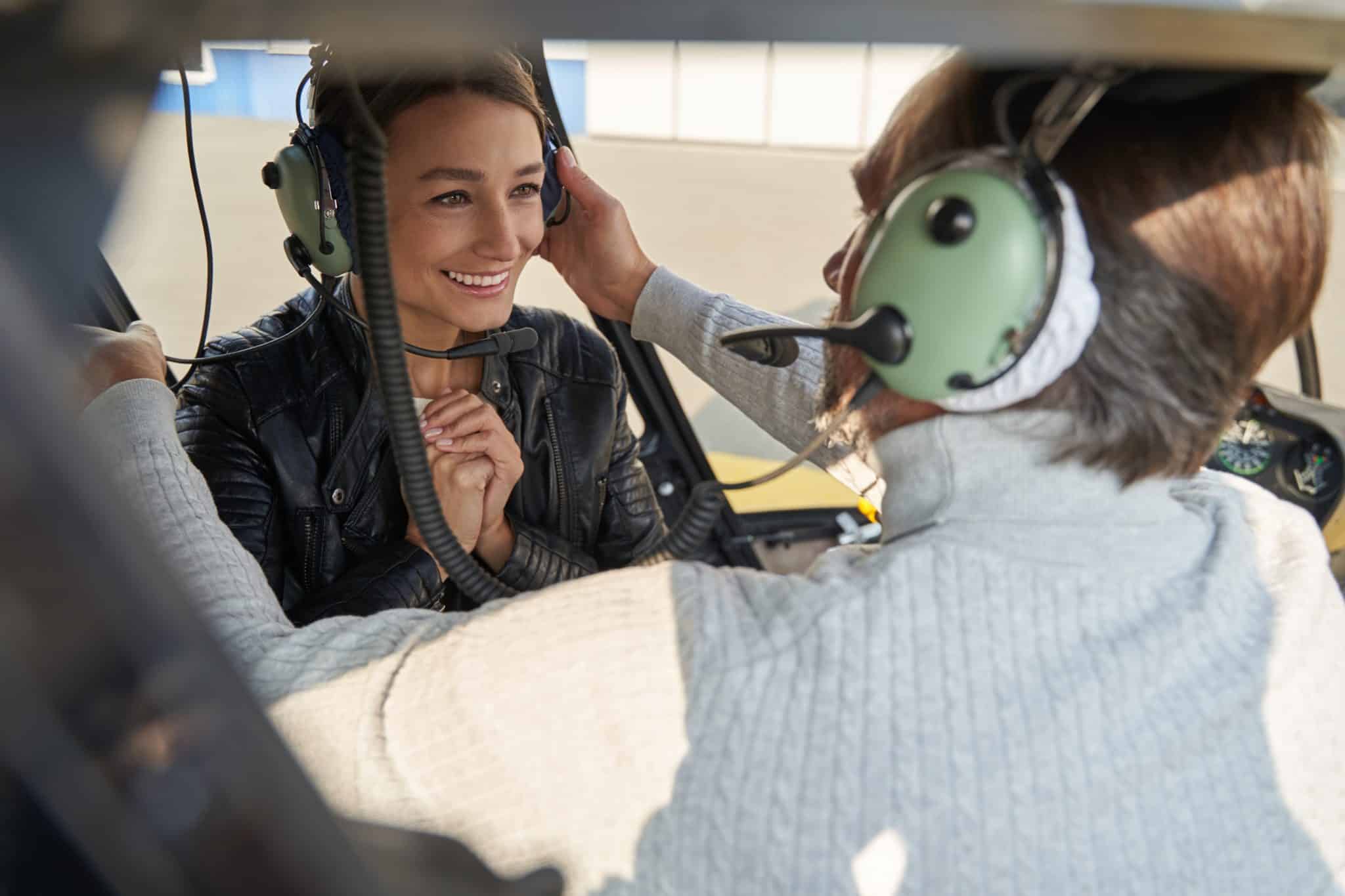 Brunette woman looking grateful while pilot helping her with aviation headset on helicopter